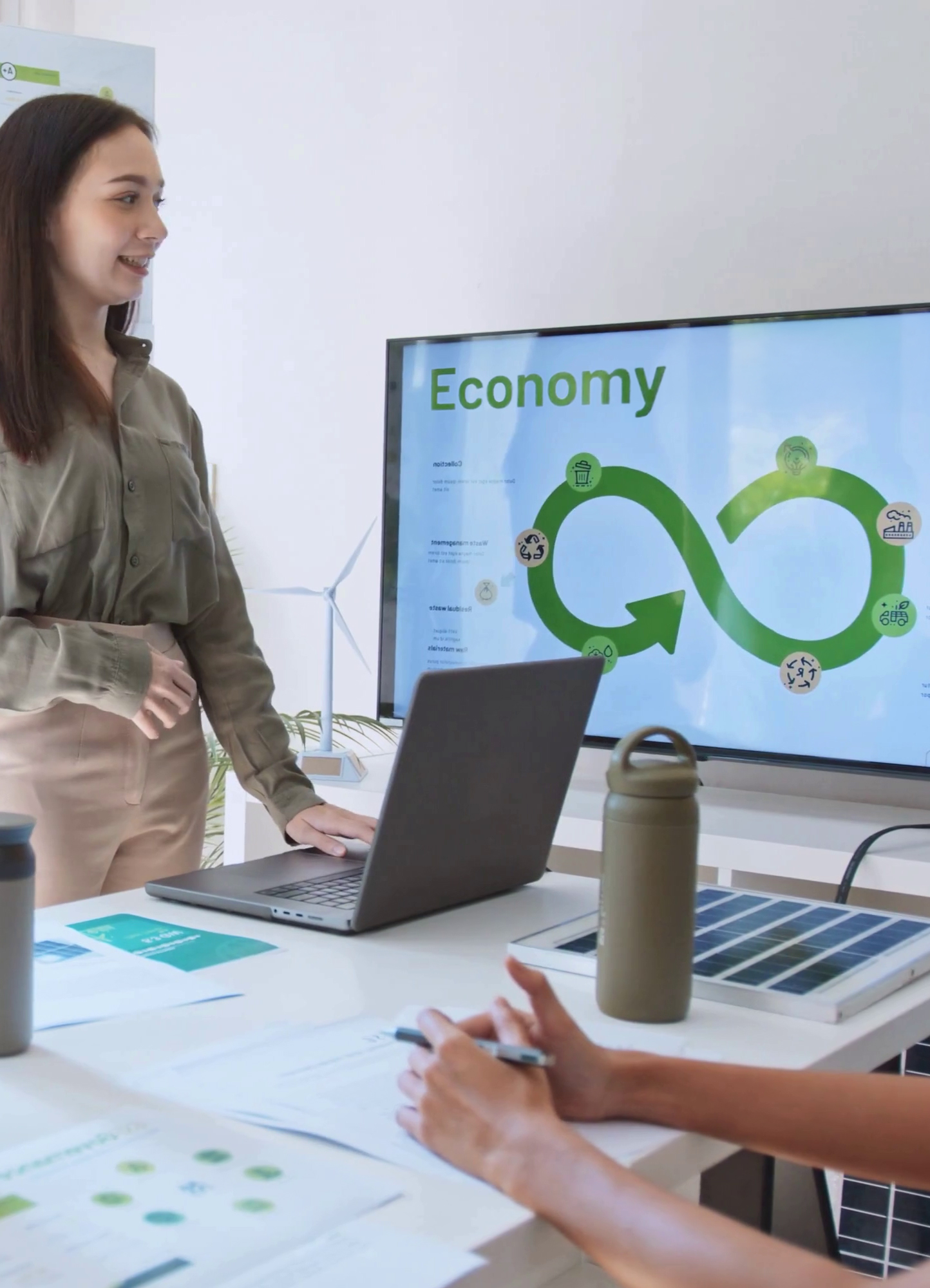 Una donna in piedi spiega un'infografica a forma di infinito su uno schermo su cui è scritto "circular economy".