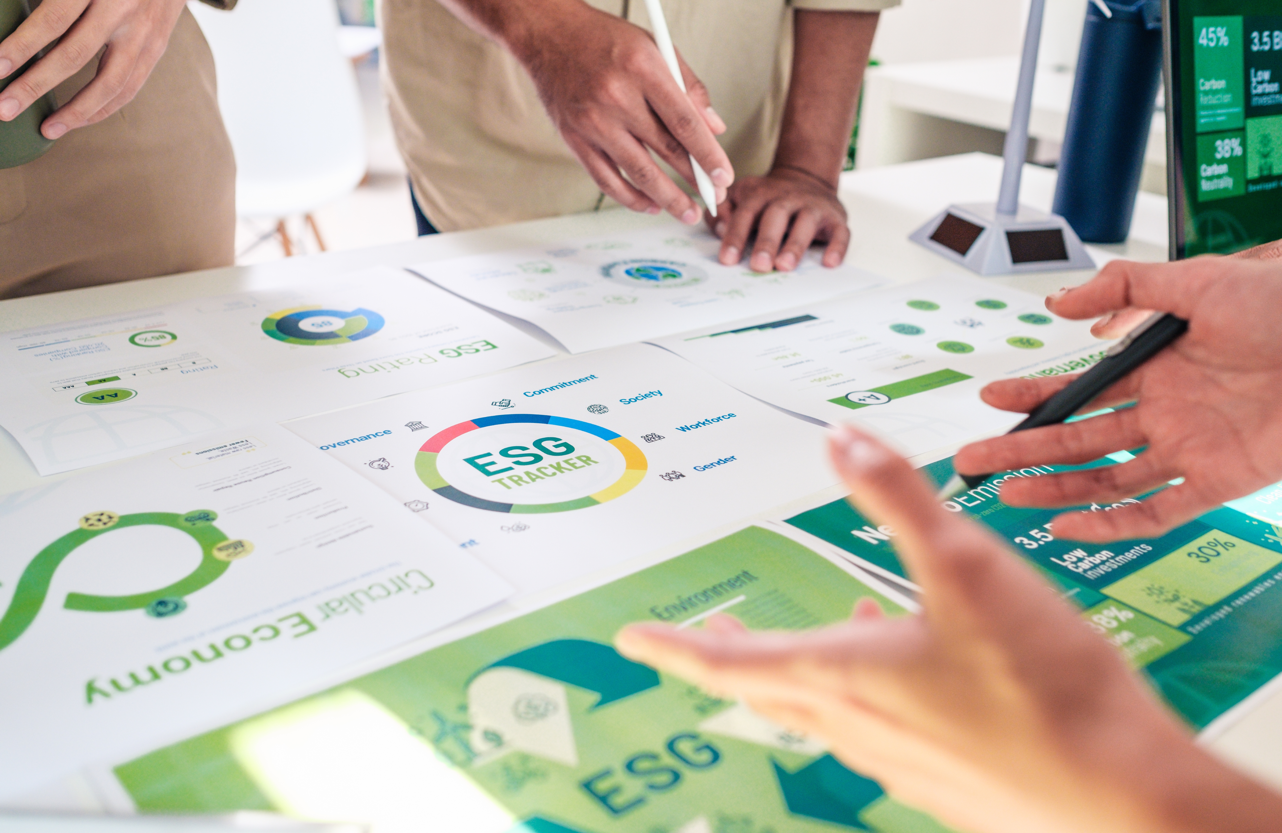 Mani di persone attorno a un tavolo ricoperto di fogli sul quale sono stampati grafici e scritte relative a ESG e circular eceonomy