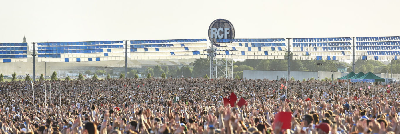 Foto di una folla numerosa durante un evento live alla RCF Arena, con il logo dell'arena visibile sullo sfondo e decorazioni blu e bianche sopra il pubblico.